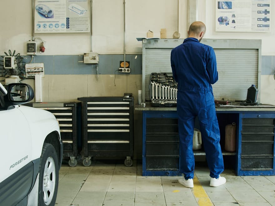 man in blue overall beside white car in service garage